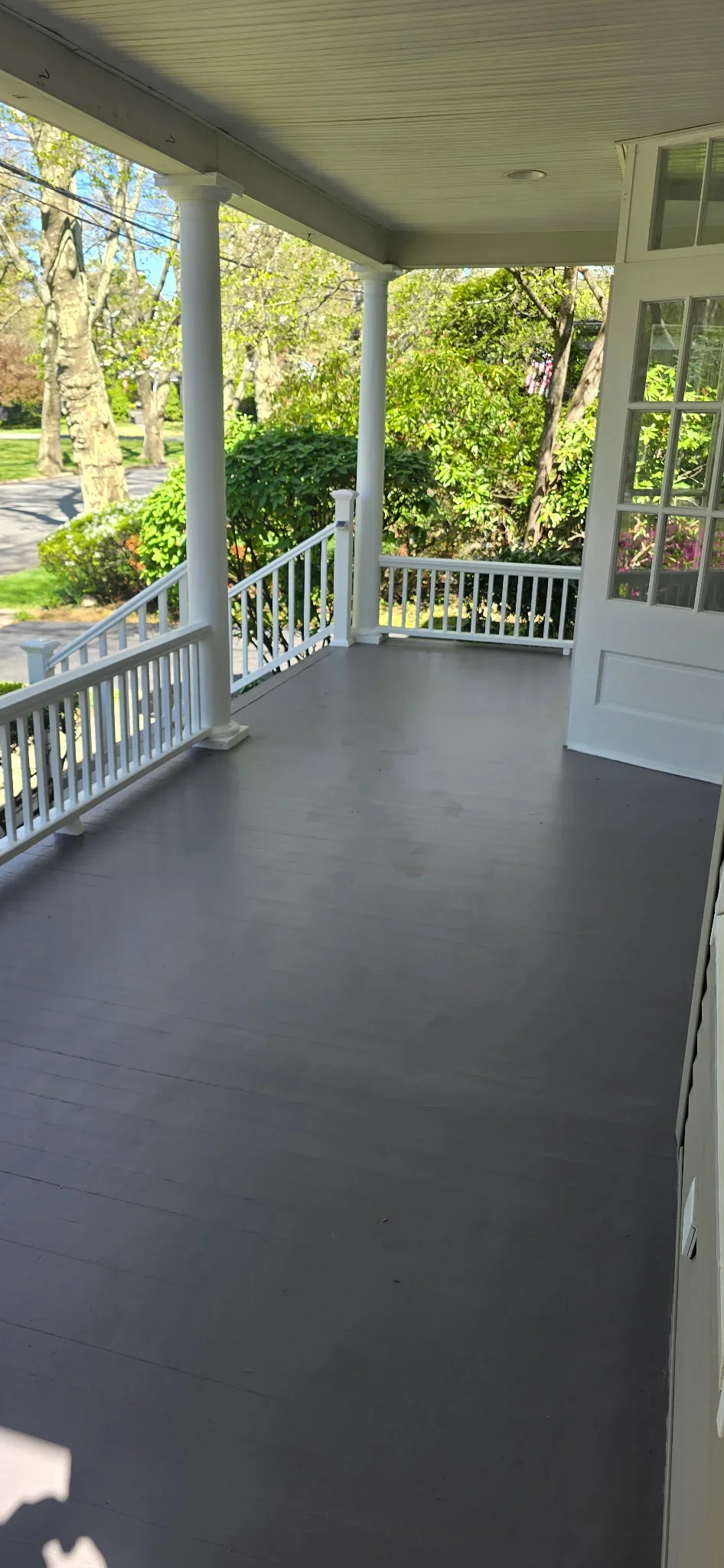 Dark composite deck with white vinyl railings and columns under covered porch roof