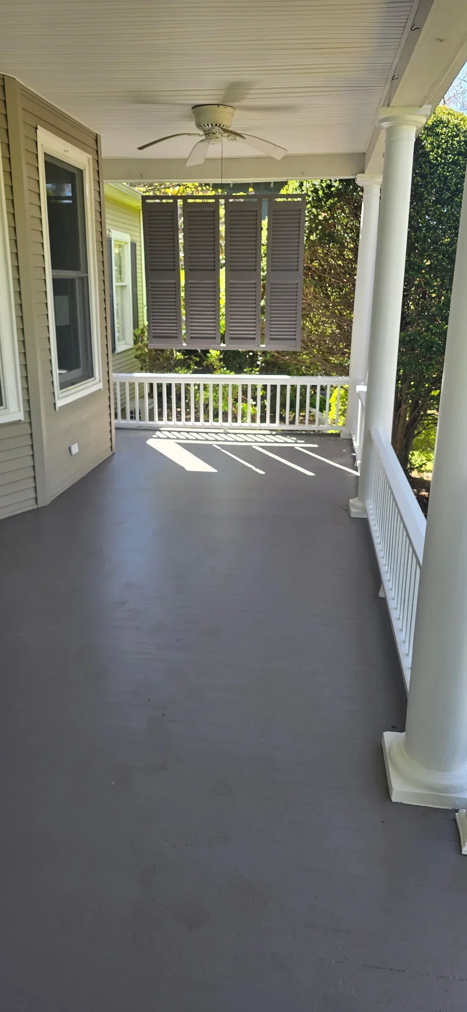 Composite deck with white railings, louvered privacy screens, and ceiling fan under covered porch
