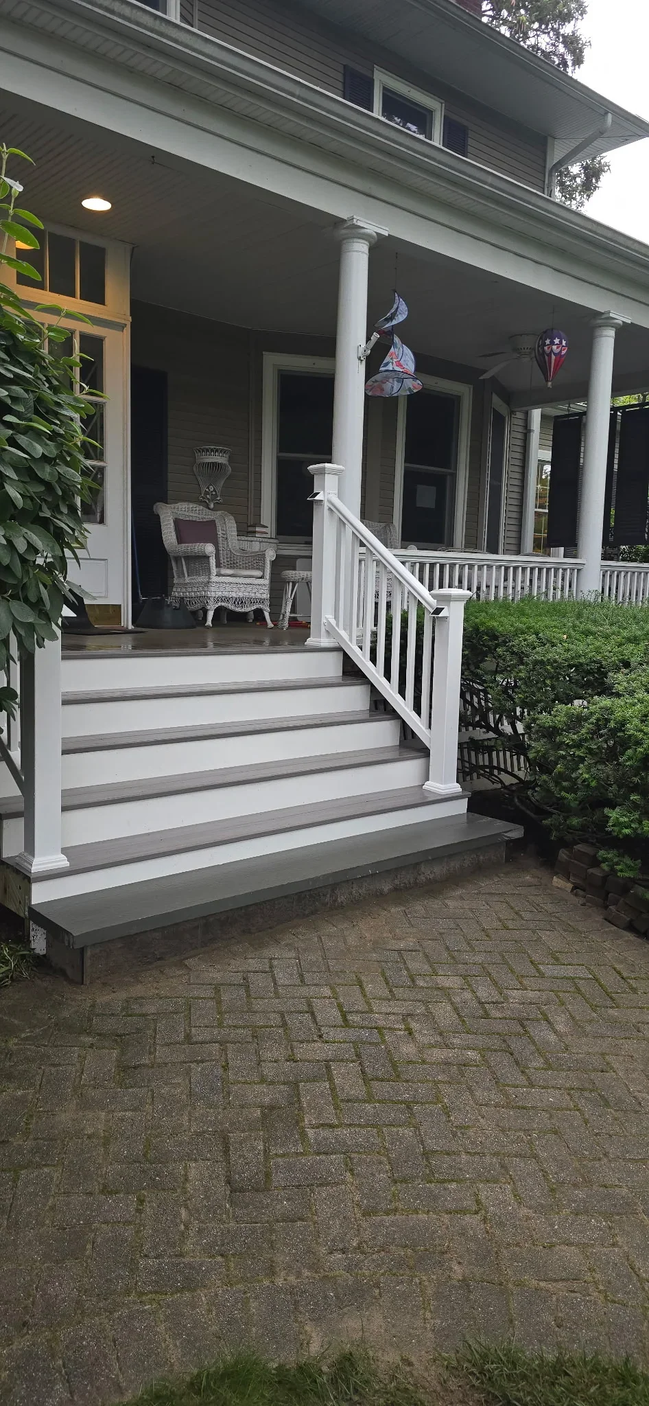 White composite deck with gray and white striped steps, vinyl railings, and support columns on front porch