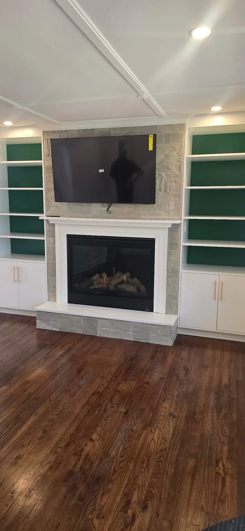 Stone fireplace with TV mount, custom built-in shelving, gas fireplace insert, and hardwood floors