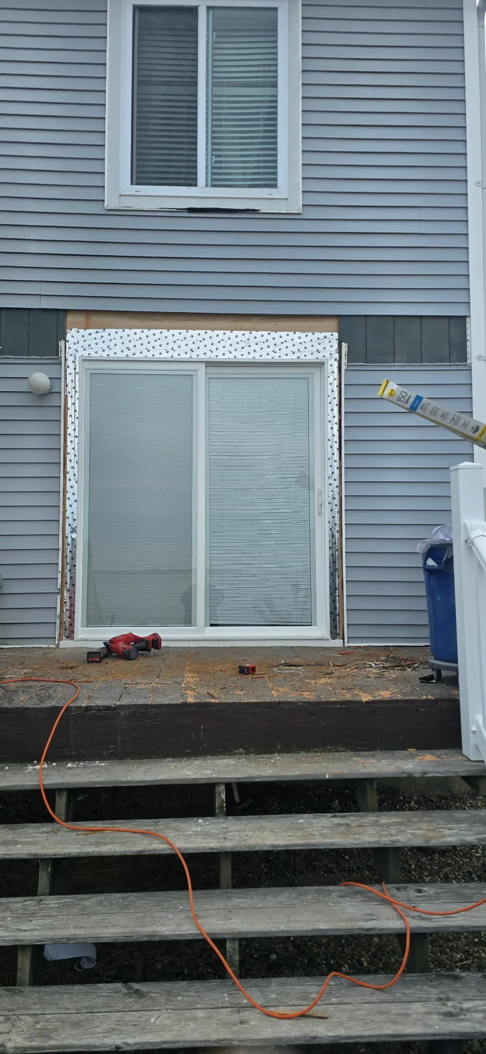 White sliding glass door with blinds installed on deck, weatherproof tape and flashing visible