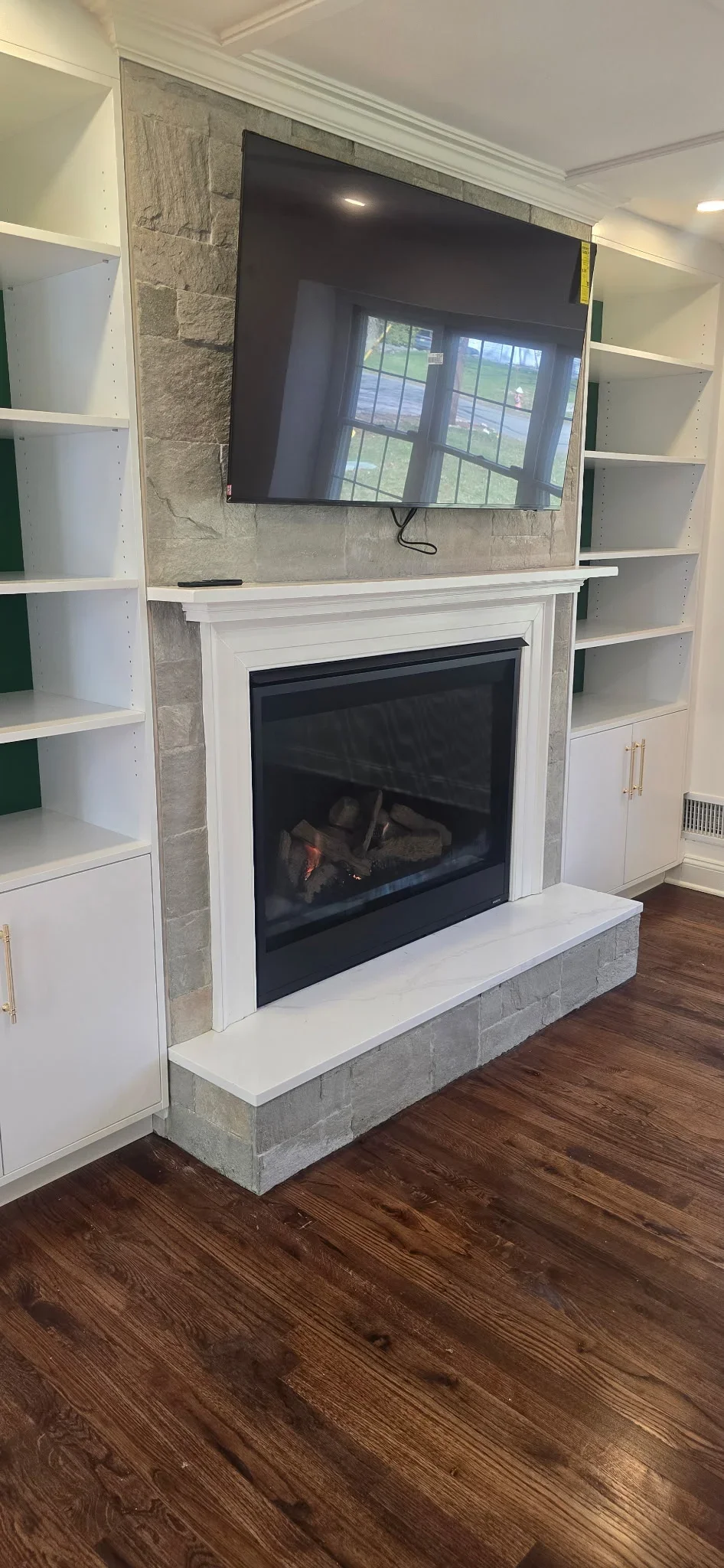 Stone fireplace with white trim, gas insert, built-in white shelving, and wall-mounted TV