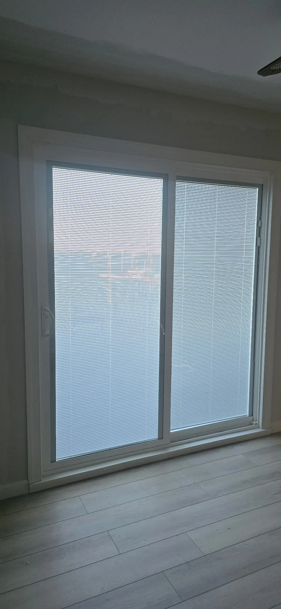 White sliding glass doors with integrated mini blinds, aluminum frame, light wood flooring