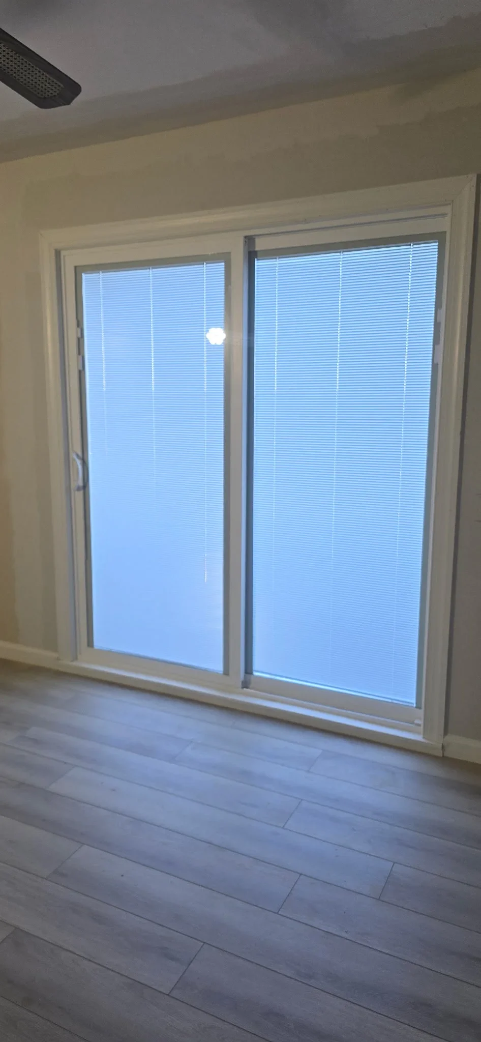 White-framed sliding glass doors with integrated blinds installed in drywall opening