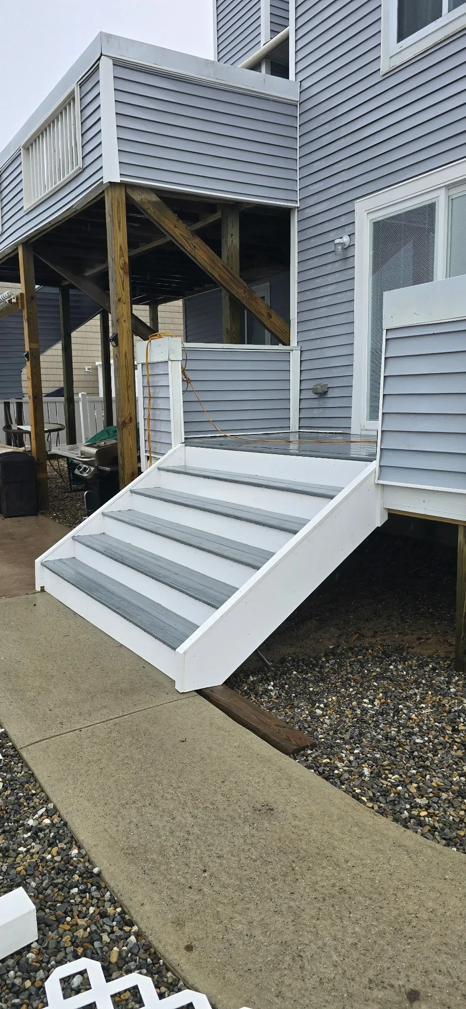 White composite deck stairs with gray treads and horizontal cable railing attached to gray siding home